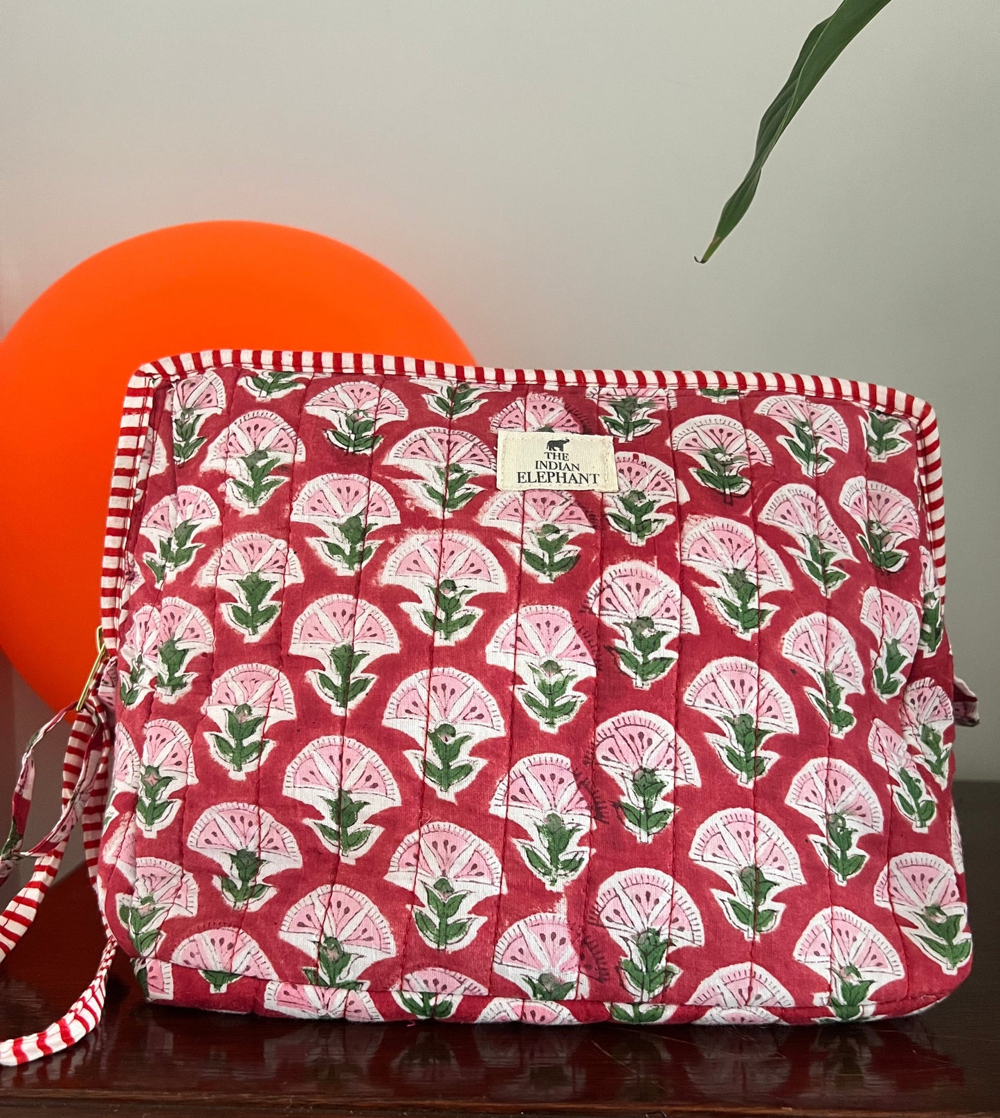Red fabric pouch with green leaf pattern on a white surface