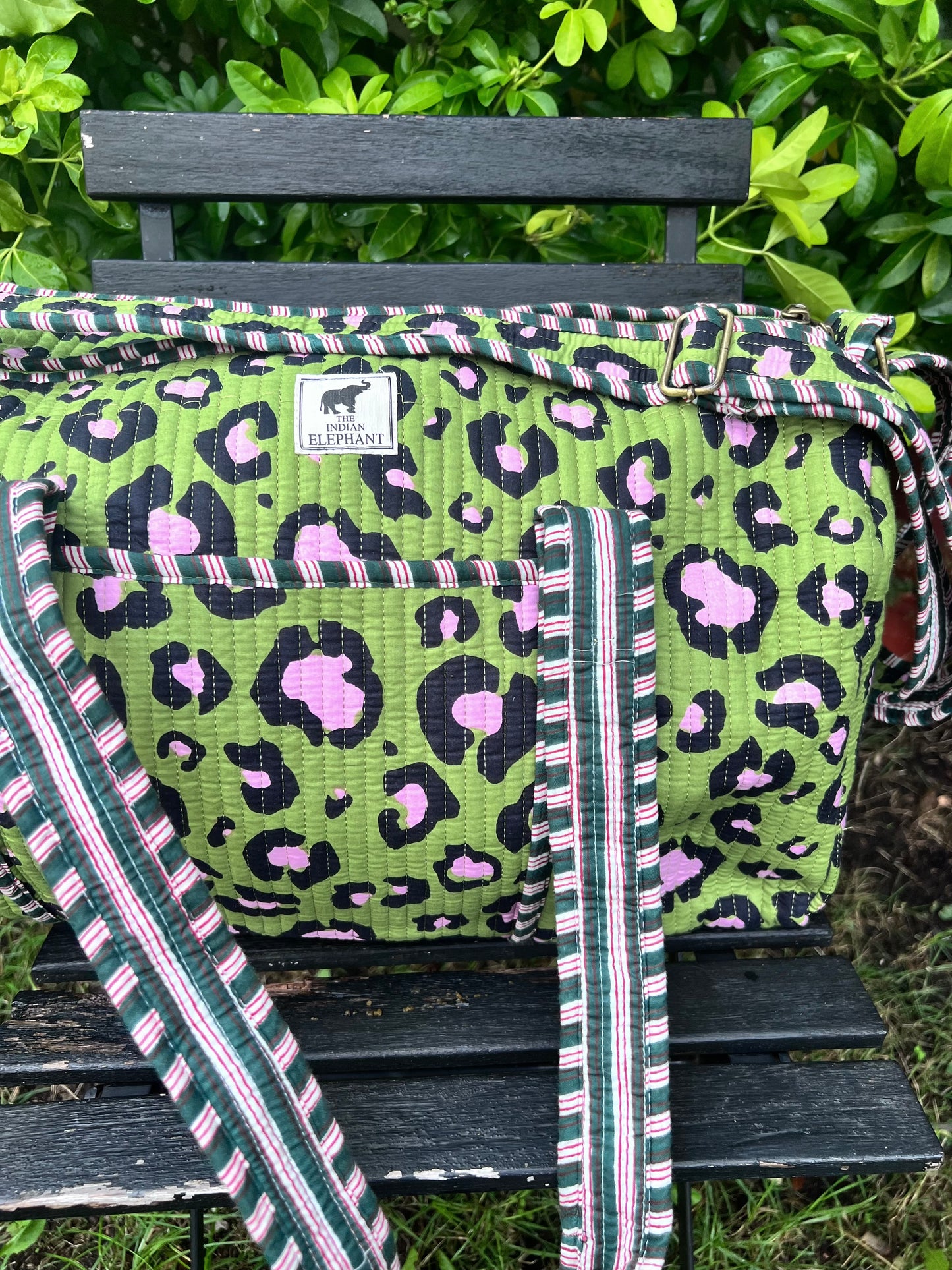 Green leopard print bag with a strap on a wooden bench outdoors