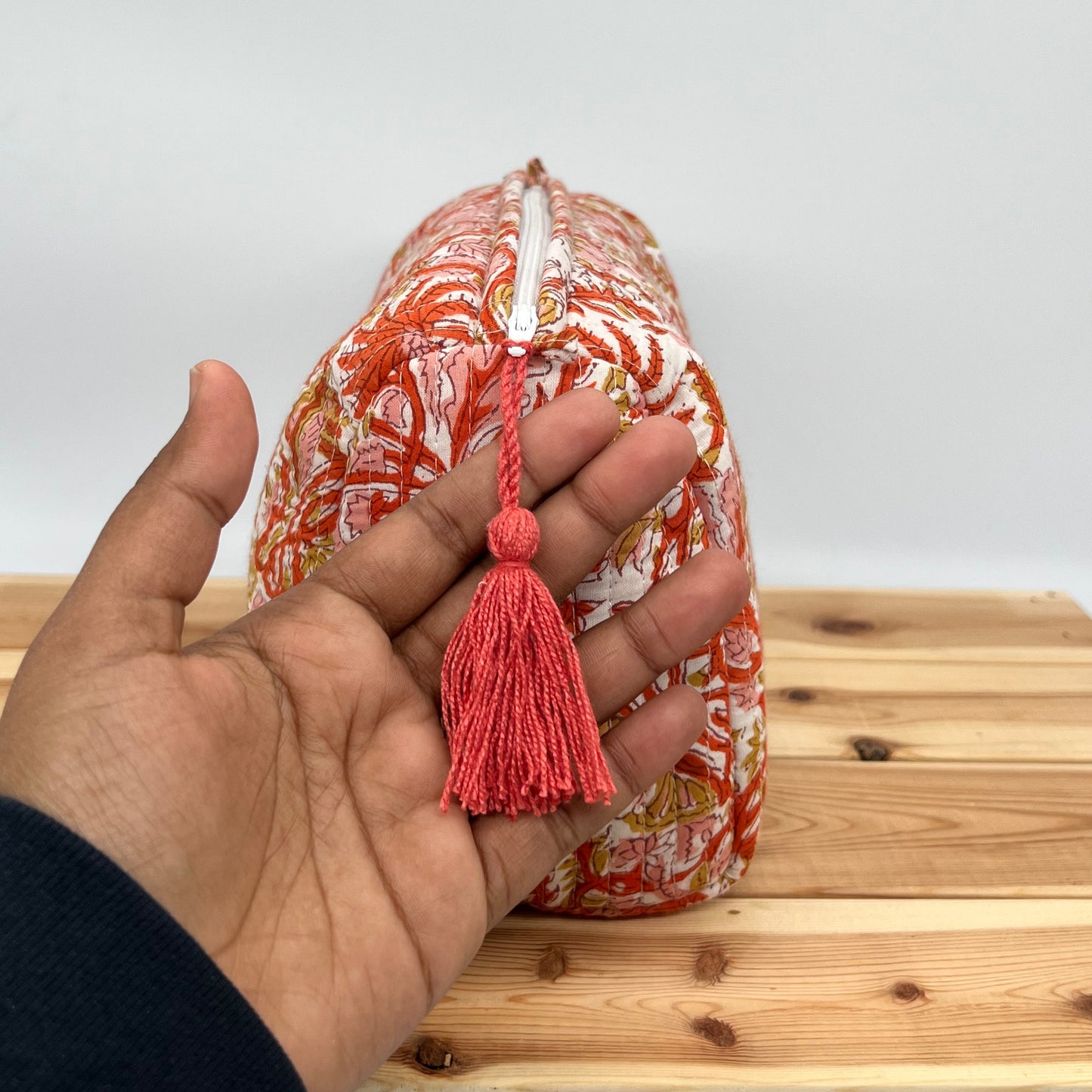 Hand holding a decorative item with a tassel against a wooden background